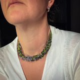 green hand knotted and felted necklace showing flameworked mini beads and mini lilac headpins. necklace worn on model.