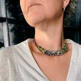 flameworked glass mini beads and lilac flower headpins strung on a hand knotted and felted necklace in purple with green felt details. shown worn on model.