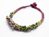 front angle detail of flameworked glass mini beads and lilac flower headpins strung on a hand knotted and felted necklace. on white background.