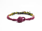 closed ball and hoop clasp detail of flameworked glass, hand knotted and felted necklace in purple. on white background.