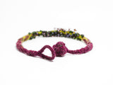 open ball and hoop clasp detail of flameworked glass, hand knotted and felted necklace in purple. on white background.