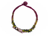 flatlay photo of entire hand knotted and felted necklace. showing flameworked glass mini beads and lilac flower headpins. necklace is purple with green felt details. on white background.