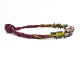 left side detail of flameworked glass mini beads and lilac flower headpins strung on a hand knotted and felted necklace in purple with green felt details. on white background.