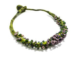 front angle detail view of a green hand knotted and felted necklace showing flameworked mini beads and mini lilac headpins. photo on white background.