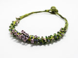 front angle detail view of a green hand knotted and felted necklace showing flameworked mini beads and mini lilac headpins. photo on white background.