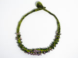 flatlay view of the entire green hand knotted and felted necklace showing flameworked mini beads and mini lilac headpins. photo on white background.