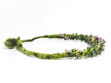 left side detail view of a green hand knotted and felted necklace showing flameworked mini beads and mini lilac headpins. photo on white background.