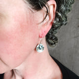 flameworked glass beads in dark charcoal are set with sterling silver and brass disks hanging on sterling silver ear hooks shown worn