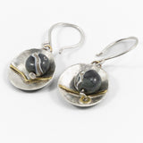 detail of flameworked glass beads in dark charcoal are set with sterling silver and brass disks hanging on sterling silver earhooks on white background.