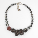 flatlay of flameworked glass necklace made with glass beads that look like wishing rocks in a dark charcoal colour. hand knotted on black silk cord with sterling silver and brass clasp shown on white background