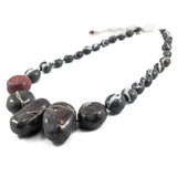 close up of central deep charcoal colour "wishing rock" beads in a flameworked glass necklace. hand knotted on black silk cord and showing the fine silver detail on the blown beads. shown on white background