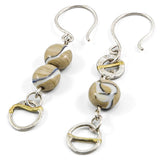 detail of flameworked glass beads in light sandstone are set with sterling silver and brass hoops, hanging on sterling silver ear hooks on white background