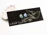 12mm flameworked glass earring studs shaped like a mussel shell in variegated colours of blues and yellows displayed on an earring card.