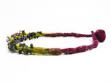 right side detail of flameworked glass mini beads and lilac flower headpins strung on a hand knotted and felted necklace in purple with green felt details. on white background.