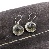 flameworked glass beads in dark charcoal are set with sterling silver and brass disks hanging on sterling silver earhooks on stone background