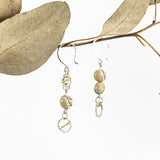flameworked glass beads in light sandstone are set with sterling silver and brass hoops, hanging on sterling silver ear hooks and shown hanging on a branch with white background