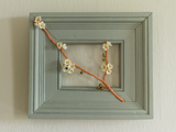 flameworked glass blossoms branch with woven copper in  wood frame on light background.