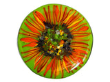 close up image of a round glass coaster showing the top design of the image of a sunflower on a bright green background. image is on a white background.
