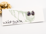 12mm mussel shell shaped flameworked glass earring studs in metallic-purple displayed on an earring card.